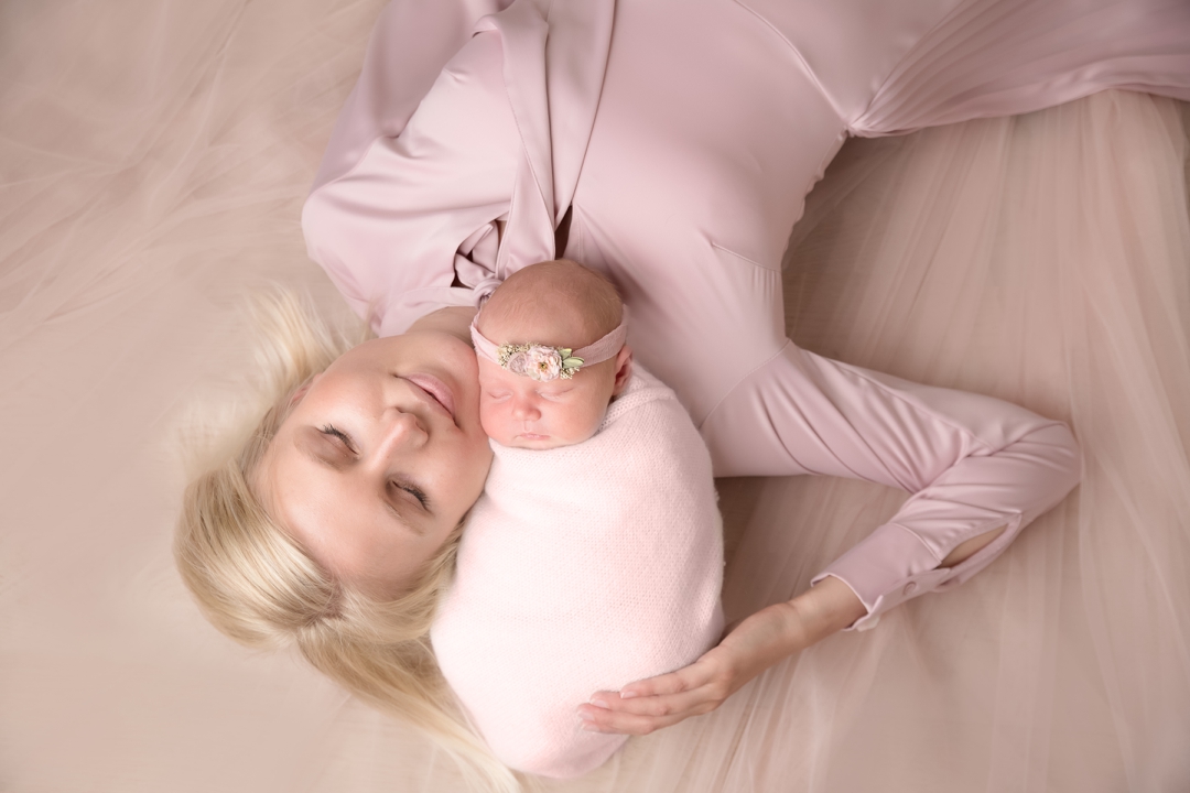 Newborn photography specialist photographer in Worcestershire. New mum in pink dress lay on soft pink tulle with her baby wrapped and posed and lay on her shoulder with her mum holding her against her head